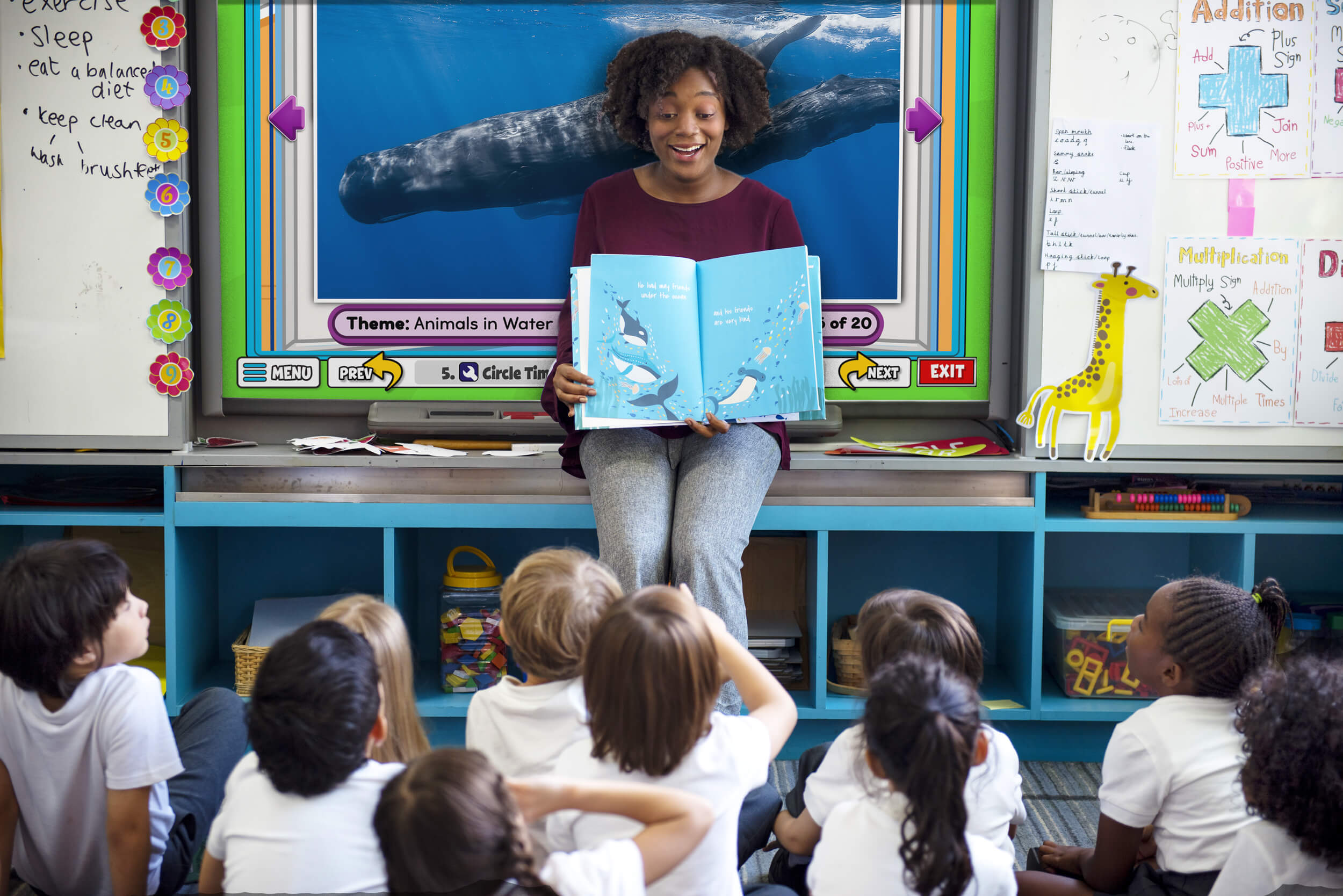 PreK teachers sits and reads to students about whales while an interactive whiteboards shows whales in the background.