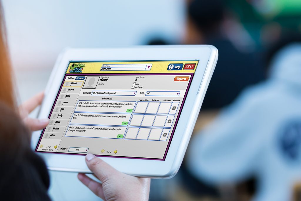 teacher hand holding use tablet with blurred student in classroo – QuaverEd Teacher hand holding a tablet with a digital assessment on the screen.