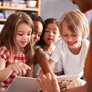 Imagen de cuatro niños sonriendo y señalando un libro en clase.
