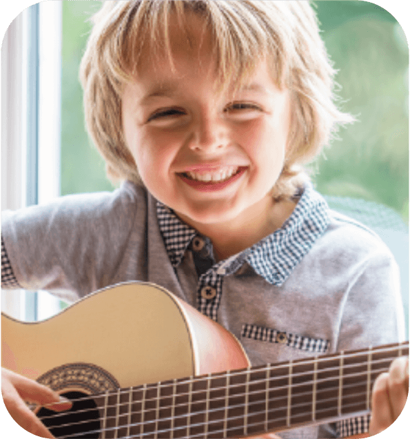 A picture of a young boy playing guitar and smiling representing the theme Music from Quaver Pre-K