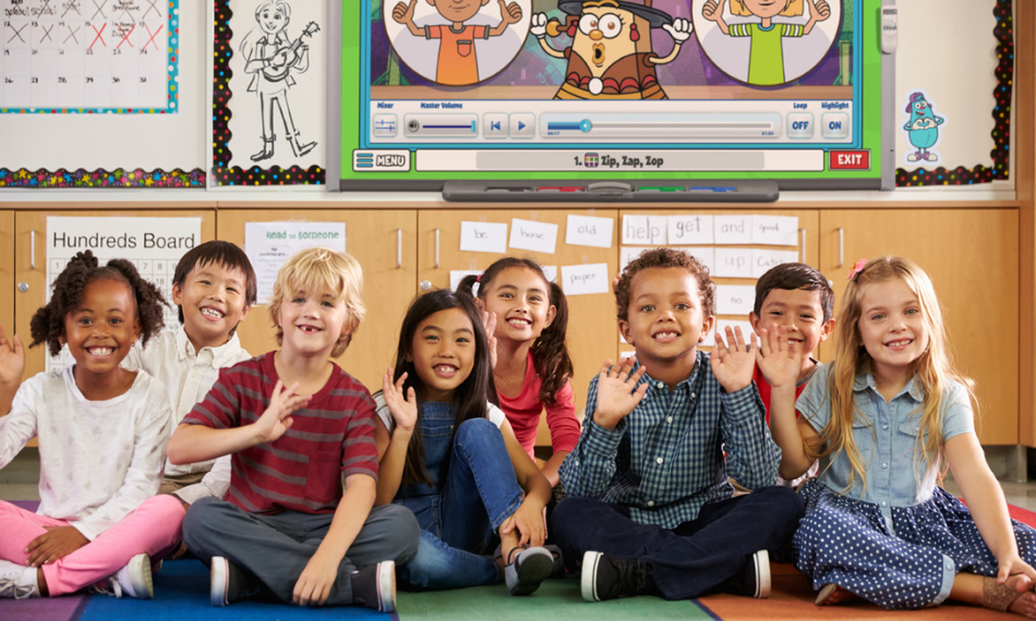 Children smiling in a classroom with Quaver Ed songs on an interactive board behind them