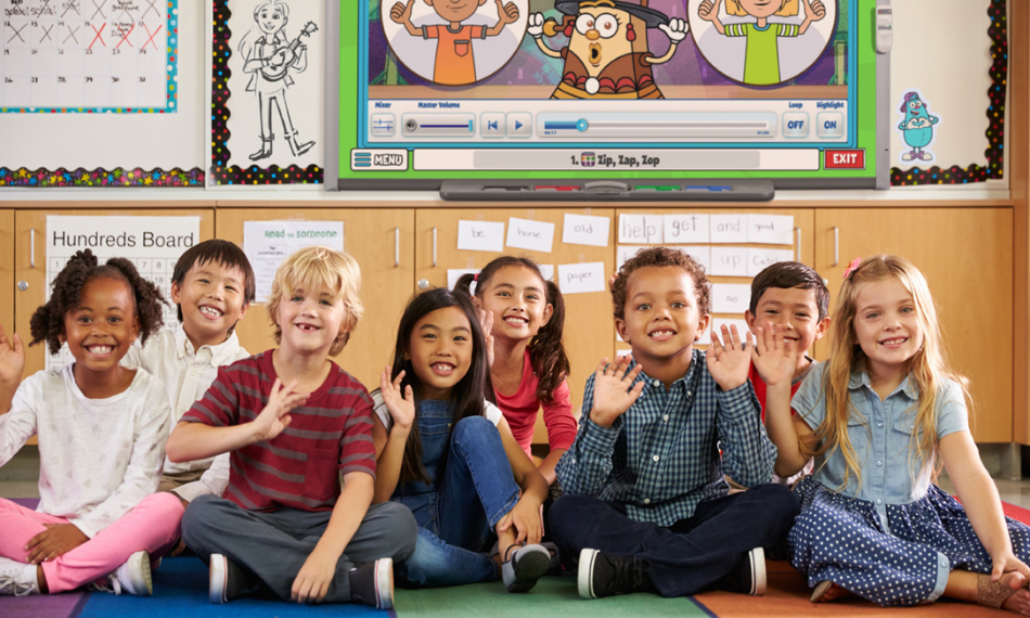 QuaverEd-products-being-used-by-kids-in-classroom – QuaverEd Children smiling in a classroom with Quaver Ed songs on an interactive board behind them