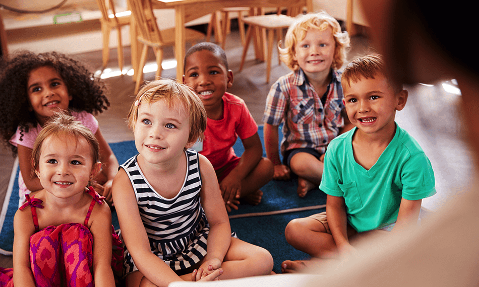 Young learners attentively listening to their teacher while smiling.