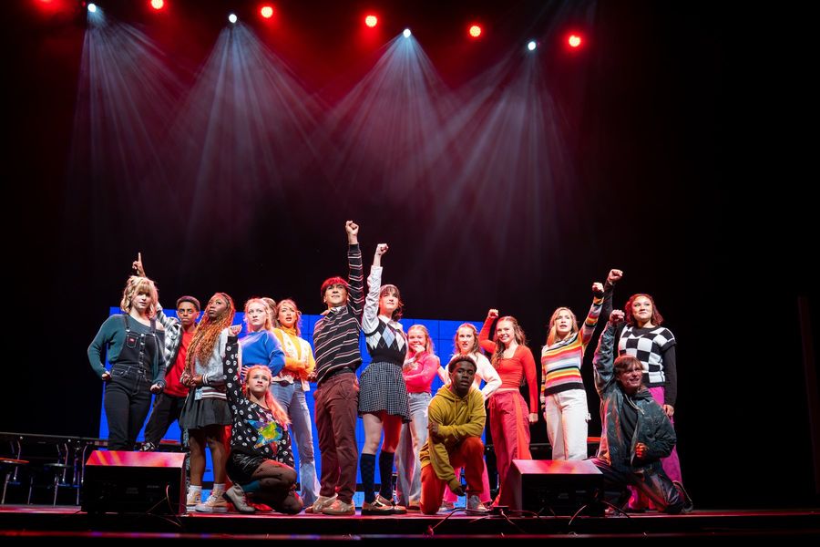 The student cast raises their fists together under red stage lights